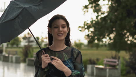 Positive-woman-in-dress-with-print-holds-umbrella-in-park