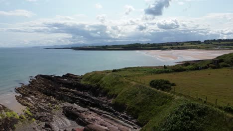 Traeth-Lligwy-idyllic-rocky-coast-shoreline-aerial-view-green-pasture-on-rocky-cliffs-edge,-descending-left-pan