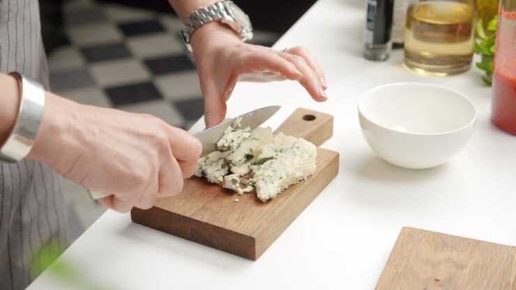 Chef che taglia formaggio erborinato su tagliere