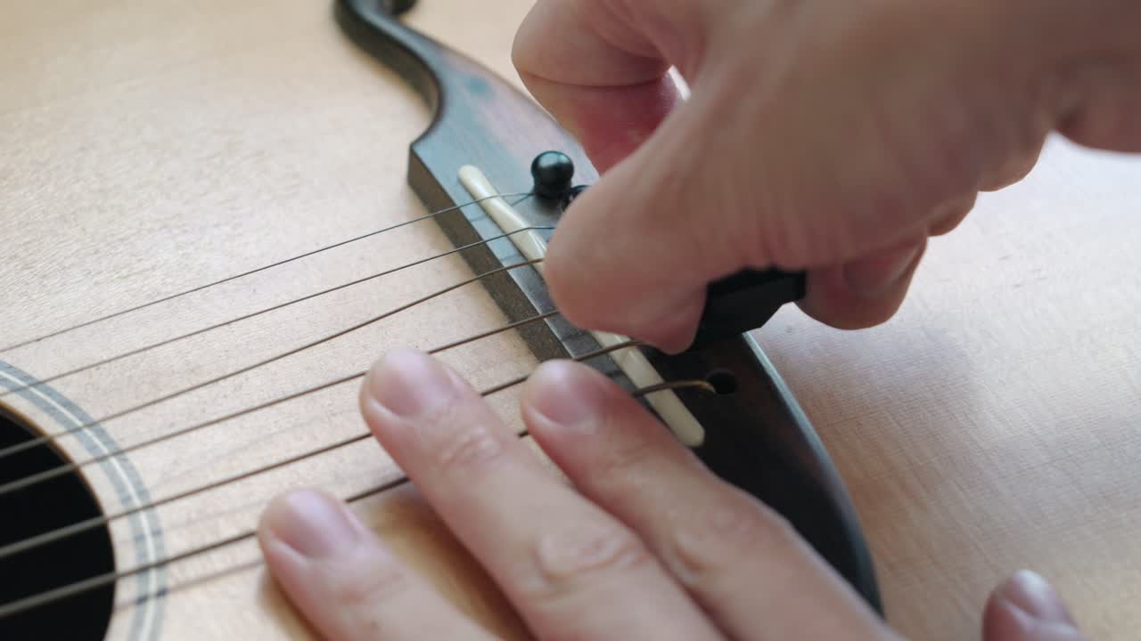 Hands Removing Bridge Pins Of An Acoustic Guitar - close up