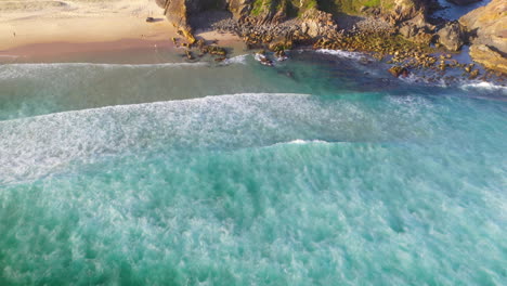 aerial shot of turquoise waves breaking on rocky coastal beach