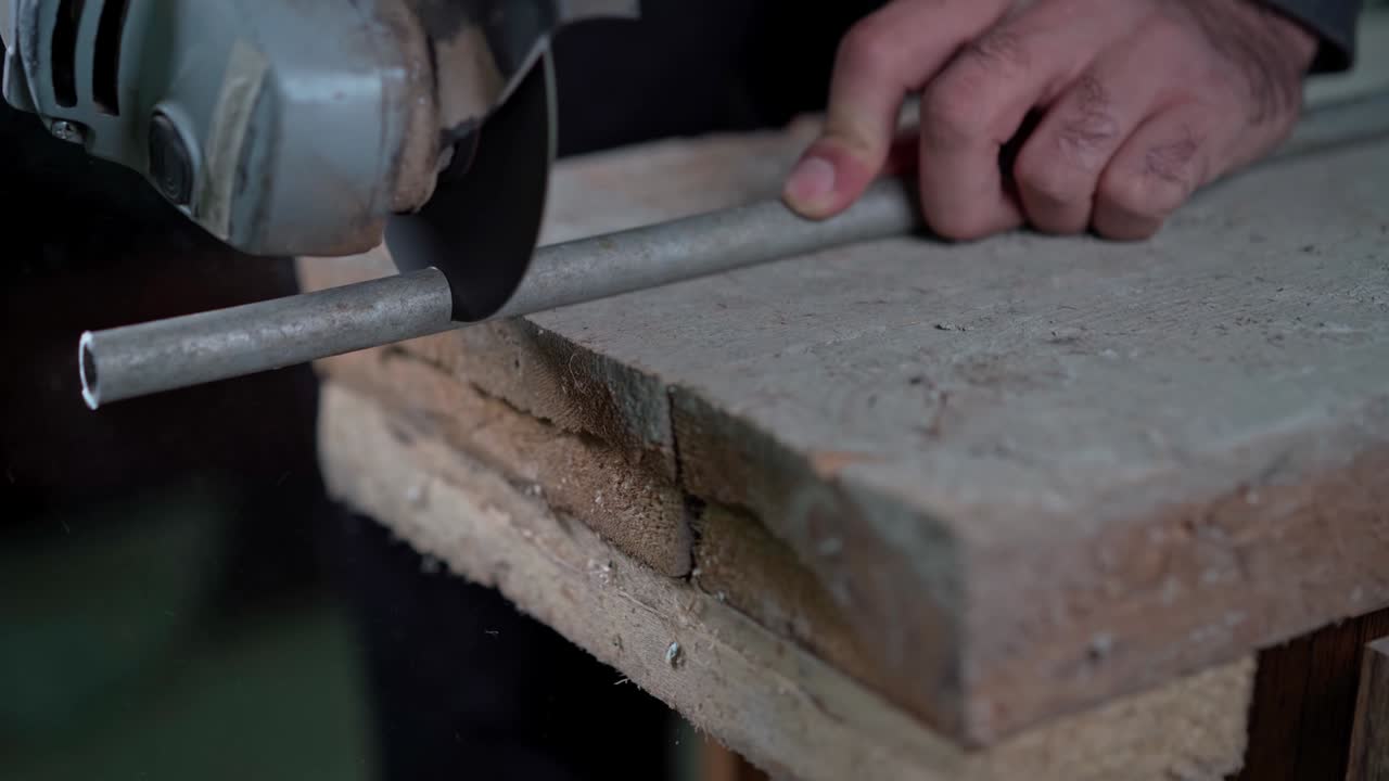 un hombre tiene una molienda de ángulo en sus manos y corta un tubo de metal con ella.