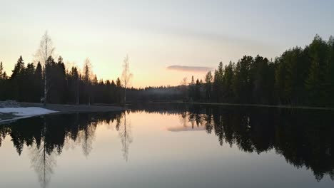 Drohne-Fliegt-über-Einen-Teilweise-Zugefrorenen-See-Mit-Einem-Sonnenuntergang-Am-Horizont-Und-Frühling-In-Der-Luft