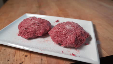 Person's-Hand-Putting-Salt-On-Top-Of-Vegan-Impossible-Burger-Patties---high-angle,-close-up