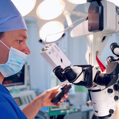 doctor with modern medical equipment. surgeon in blue uniform and mask looking into the microscope in the operating room.