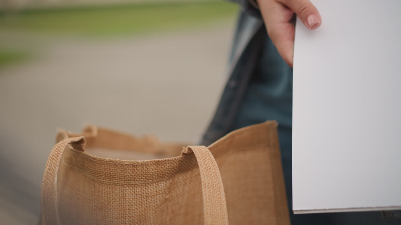 Urban message exchange. Person placing letter into tote during errands. Close shot of hand inserting envelope into bag scene. Scene of person carefully inserting letter into bag amidst city errands