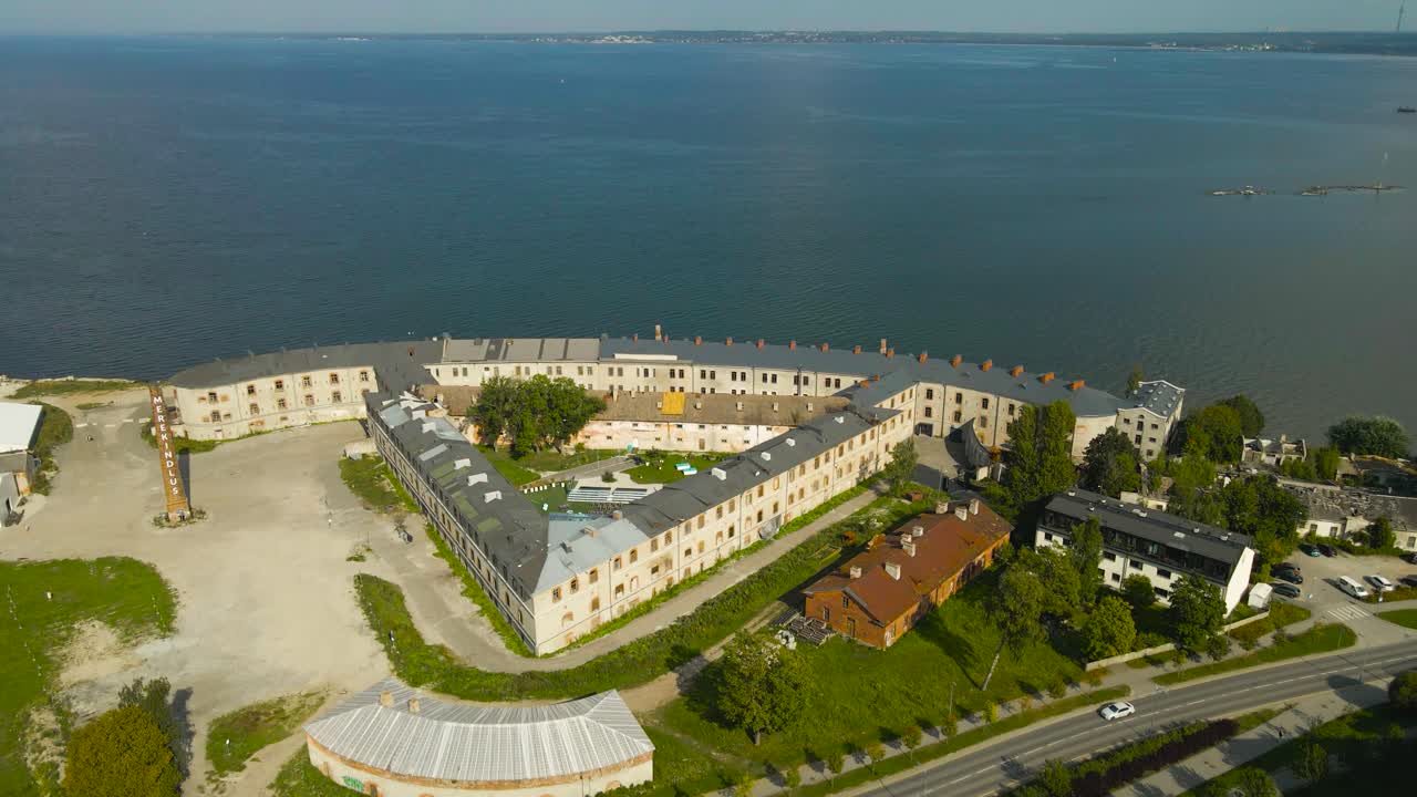 Aerial drone footage of a large former prison complext at Baltic sea shoreline called Patarei prison during summer sunny day. The sea fortress is besides blue ocean and horizon visible in the back