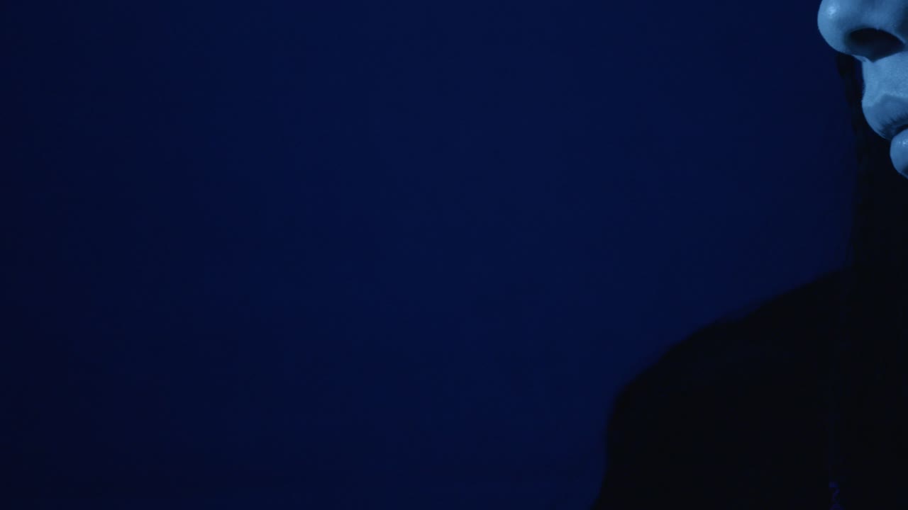 Close-up of a woman's contemplative profile in dramatic blue lighting, highlighting intricate braids and expressive features, creating an intimate and artistic atmosphere