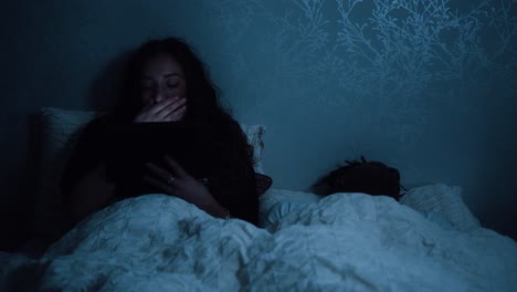 mujer cansada bostezando mientras ve su dispositivo tableta en la cama por la noche