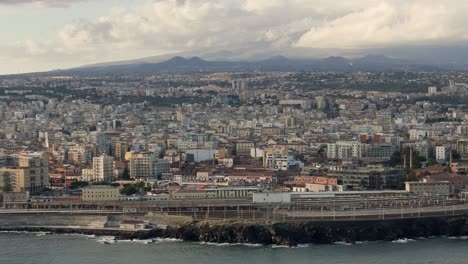 Ciudad-De-Catania,-Sicilia-Con-El-Monte-Etna-Al-Fondo,-Drone-Estableciendo-Una-Cálida-Luz-De-La-Tarde