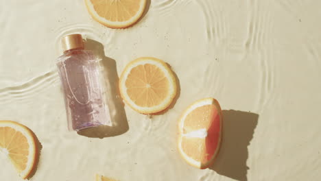 video of beauty product bottle and orange slices in water with copy space on yellow background