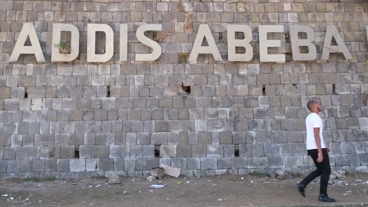 African American man walking past a stone wall with the city name Addis Abeba, Ethiopia, exploring his roots and connecting with heritage in the capital city, sow motion shot