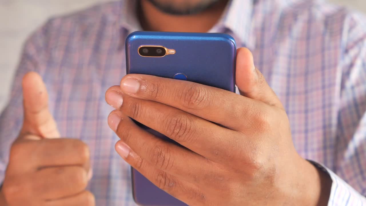 파란색 스마트폰을 들고 엄지손가락을 올리는 사람