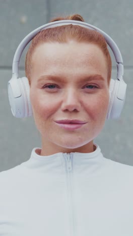 a confident woman in a sleek white athletic outfit puts on her headphones, embodying focus and readiness for her workout or fitness journey, with a serious yet inspiring expression