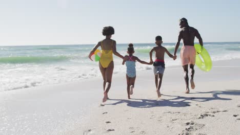 smiling african american family holding hands and running on sunny beach