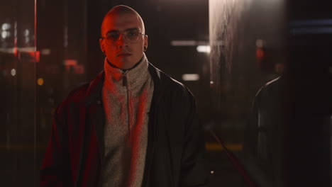 portrait of a bald man with glasses in red lit urban setting at night
