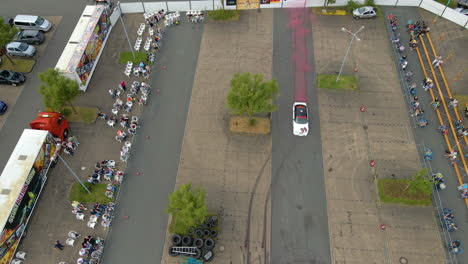 Vista-Aérea-Del-Camión-De-Deriva-Blanca-Que-Emite-Humo-De-Colores-Durante-La-Exhibición-De-Autos-En-La-Arena