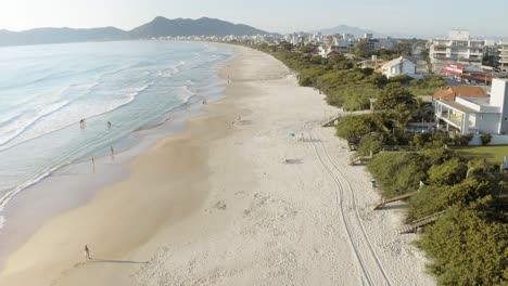 drone volando sobre una playa con olas rodando - paisaje costero con montañas en el fondo de una playa paradisíaca tropical con arena blanca y agua azul del océano brasileño