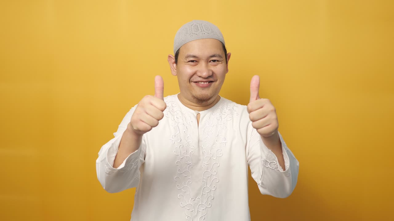 joven musulmán asiático feliz muestra el pulgar hacia arriba gesto, sonrisa cara feliz, aprobado ok signo, contra fondo amarillo