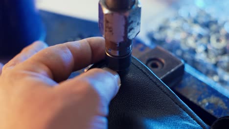 closeup view of hands of leather craftsman attaching metal round snaps to clothes with help of special machine at garment factory