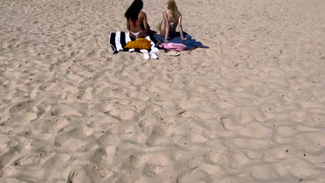 two gorgeous young women wearing bikinis strolling along the edge of the sea on a tropical beach chatting in caparica beach