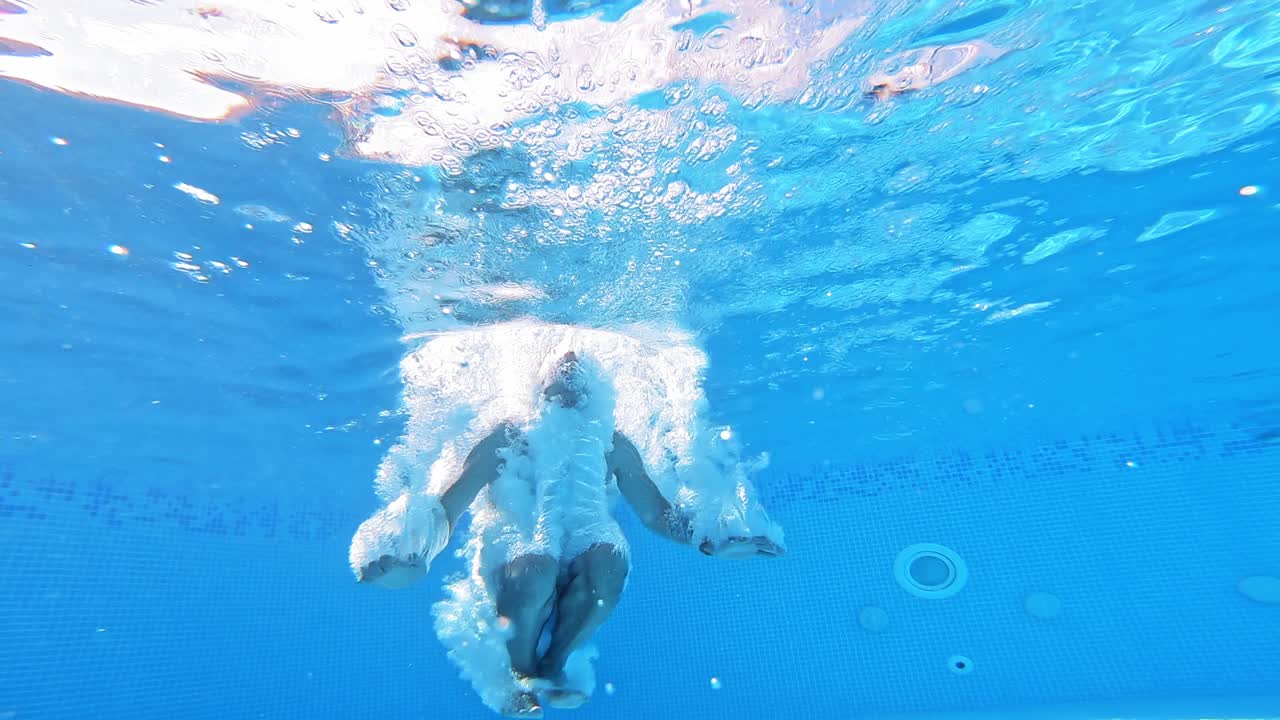 An energetic dive into a swimming pool. Handsome young man swimming in pool, underwater view