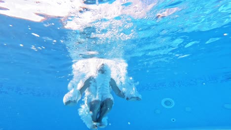 An energetic dive into a swimming pool. Handsome young man swimming in pool, underwater view