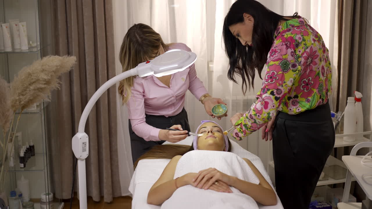 Three women in a beauty salon, one receiving a facial skincare treatment