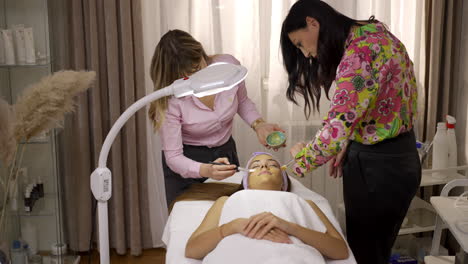 three women in a beauty salon, one receiving a facial skincare treatment