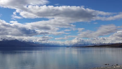 Slow-static-zoom-towards-beautiful,-clear-water-of-alpine-lake-with-majestic-mountains-in-distance