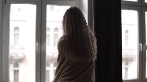 Carefree-woman-dances-against-the-background-of-the-large-windows-of-her-apartment-in-the-morning-in-plaid