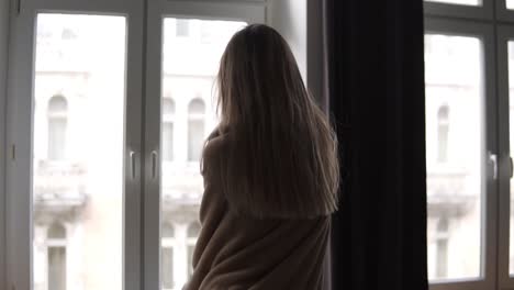 무관심 한 여자 는 아침 에 플레이드 를 입은 아파트 의 큰 창문 의 배경 에 춤 을 춘다