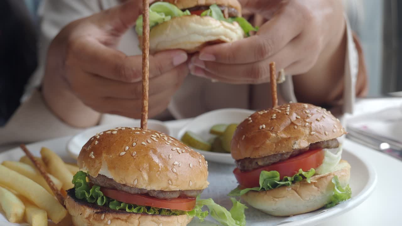 Close-up of hands serving or enjoying mini burgers and french fries