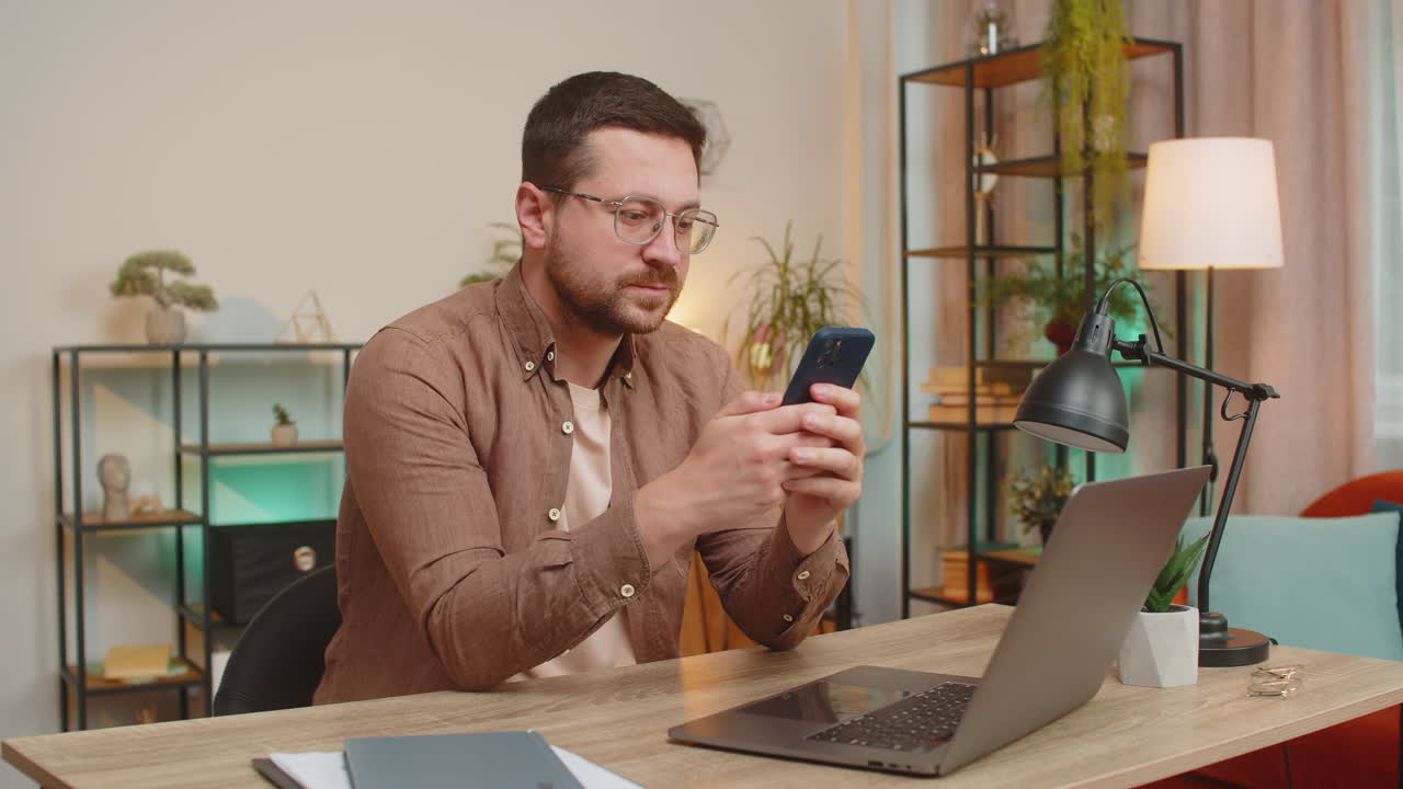 Happy young man freelancer using mobile phone celebrating success victory winning lottery at table