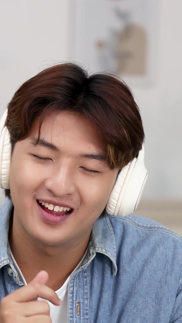 Primo piano di un uomo asiatico felice in camicia di jeans che canta indossando cuffie wireless