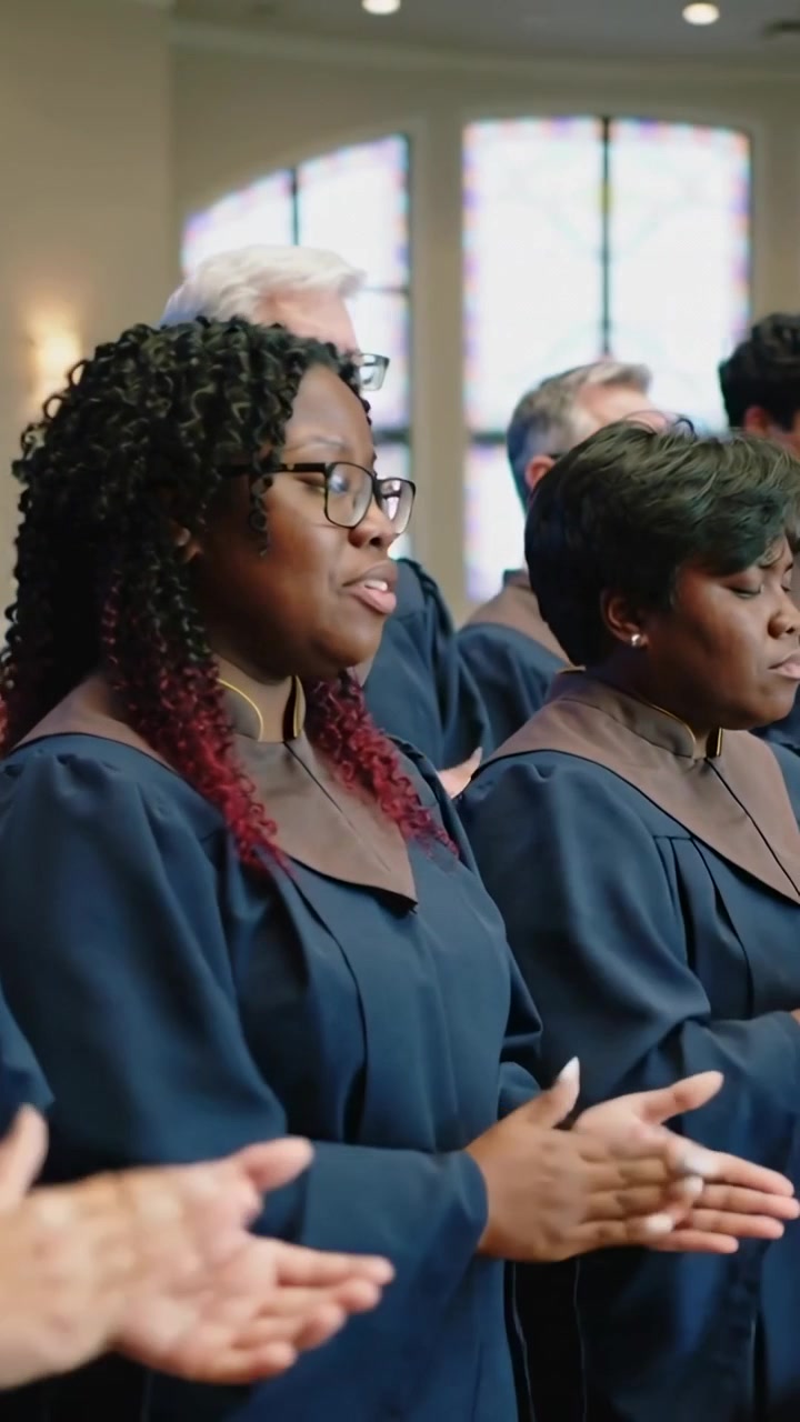 Video verticale: Corista a sinistra che applaude, con tunica blu scuro e carré marrone, al segnale del canto in chiesa, con spazio per il testo.