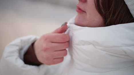 manicured hand closing up zip on plush white winter coat with gleaming silver nails, close detail shot of textured quilted fabric under soft natural light capturing warmth style in cold motion