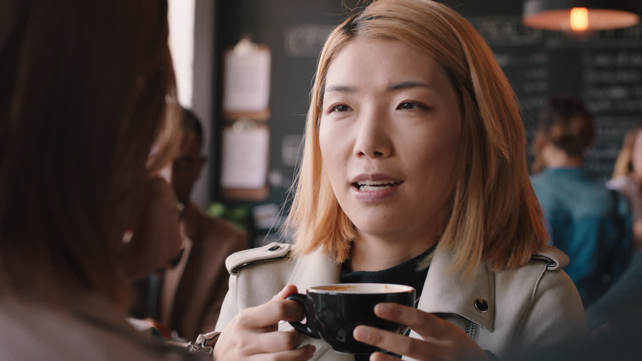 아름다운 아시아 여성이 카페에서 친구와 채팅하고 커피를 마시고 사교를 즐기고 바쁜 레스토랑에서 대화를 나누고 있습니다.