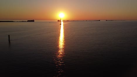 Beautiful-aerial-vibrant-high-contrast-sunset-over-calm-Baltic-sea,-distant-sailing-boat,-rock-pier-at-Port-of-Liepaja-,-wide-angle-drone-shot-moving-left