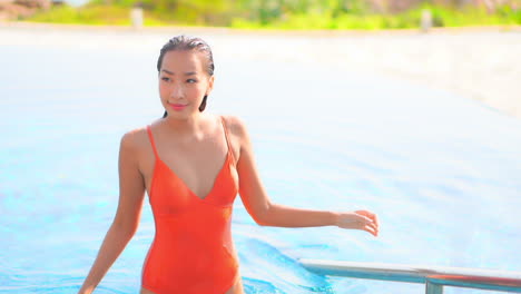 fit attractive asian woman walking out of pool runs hands over hair and body