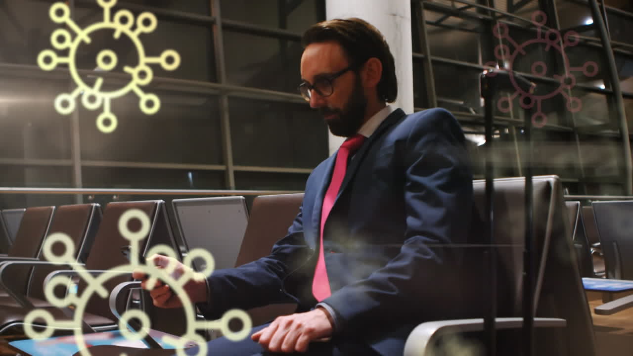 animación de iconos flotantes de células de covid-19 sobre un hombre biracial usando un teléfono inteligente en el aeropuerto