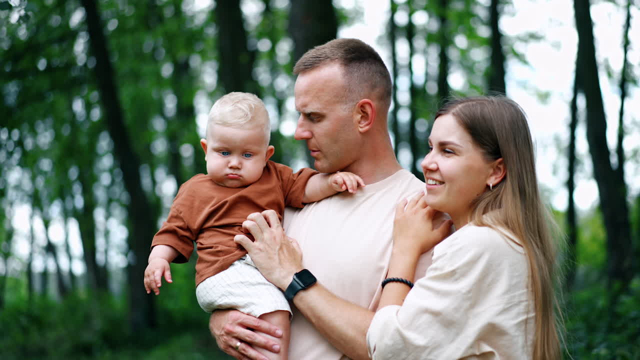 Young Caucasian parents with their little baby boy. Kid looks down intently and dad tries to attract son's attention.