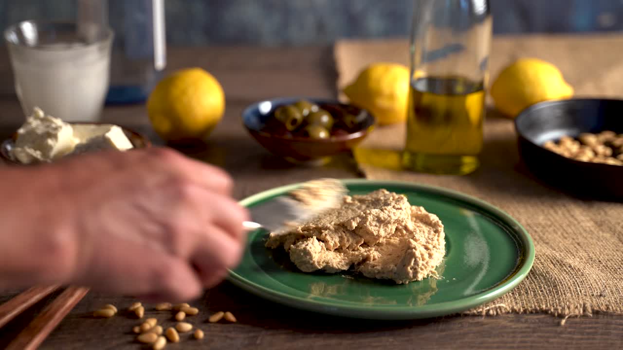 Splendida ambientazione di cibo mediorientale mentre una mano spalma l'hummus su un piatto, versa olio d'oliva e spolvera la paprika