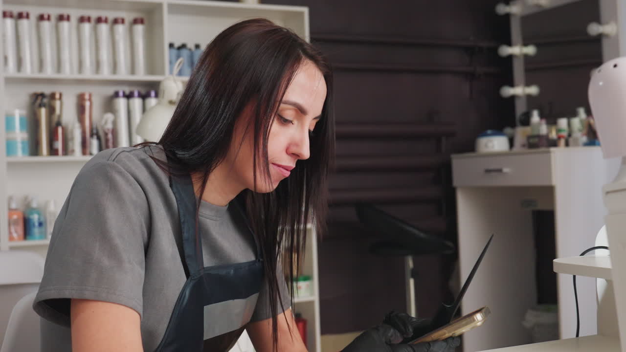 Profesional de la belleza actualizando los datos de un cliente en un dispositivo digital en el trabajo; peluquero centrado en la programación digital y el mantenimiento de registros en un entorno de salón profesional.