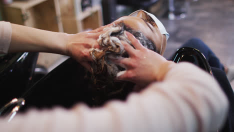 female hairdresser washing hair of female customer wearing face mask at hair salon