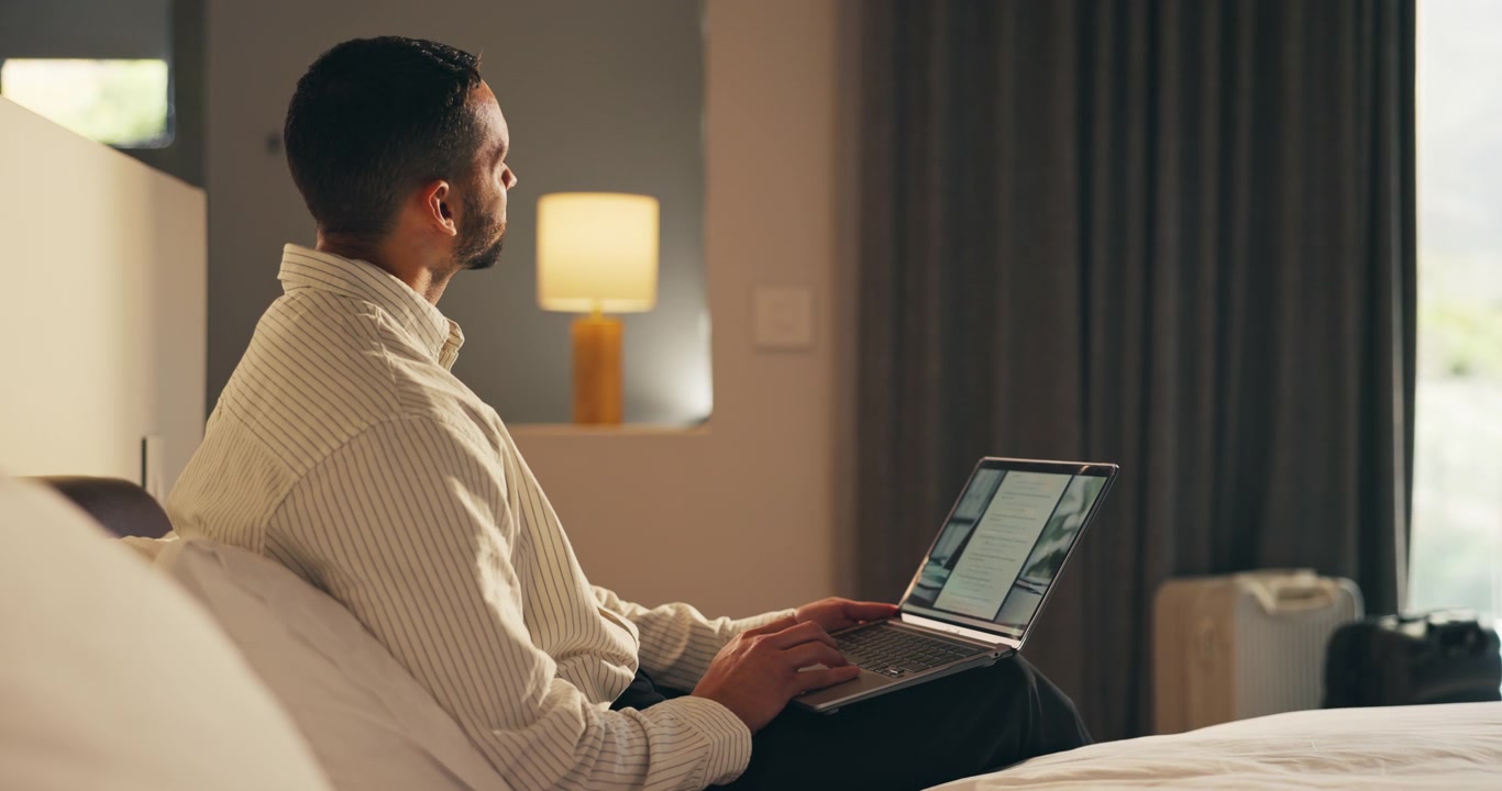 Man Working on Laptop While Sitting on Hotel Bed