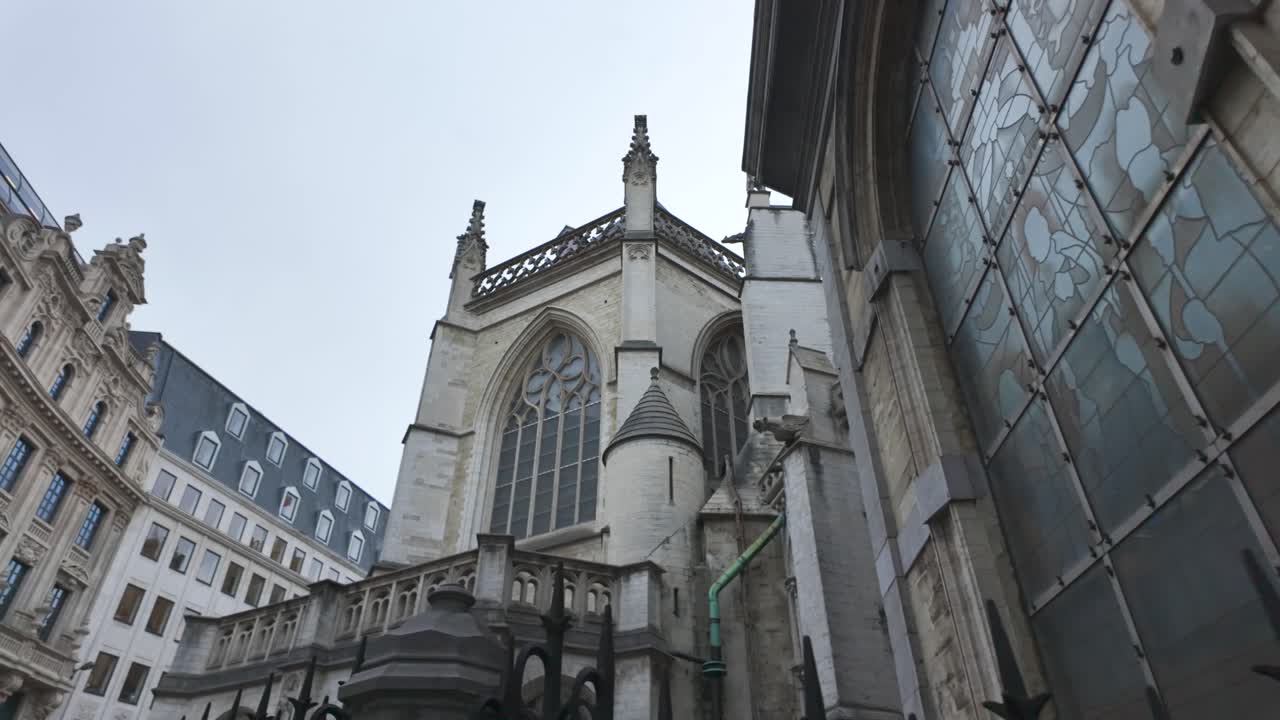 A low angle perspective of St. Michael and St. Gudula Cathedral, emphasizing its gothic details and towering spires, reveal behind wall
