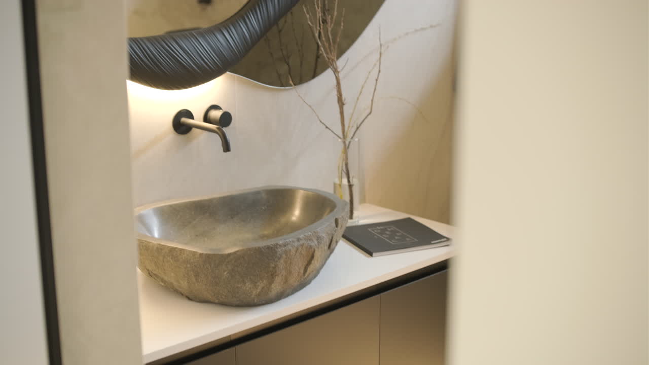 Salle de bain élégante avec vasque en pierre et miroir irrégulier.