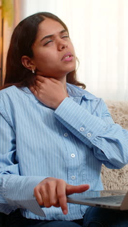 indian woman massaging neck with tired face after long laptop use on home sofa showing work strain