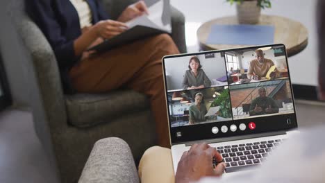 African-american-man-using-laptop-for-video-call,-with-diverse-business-colleagues-on-screen